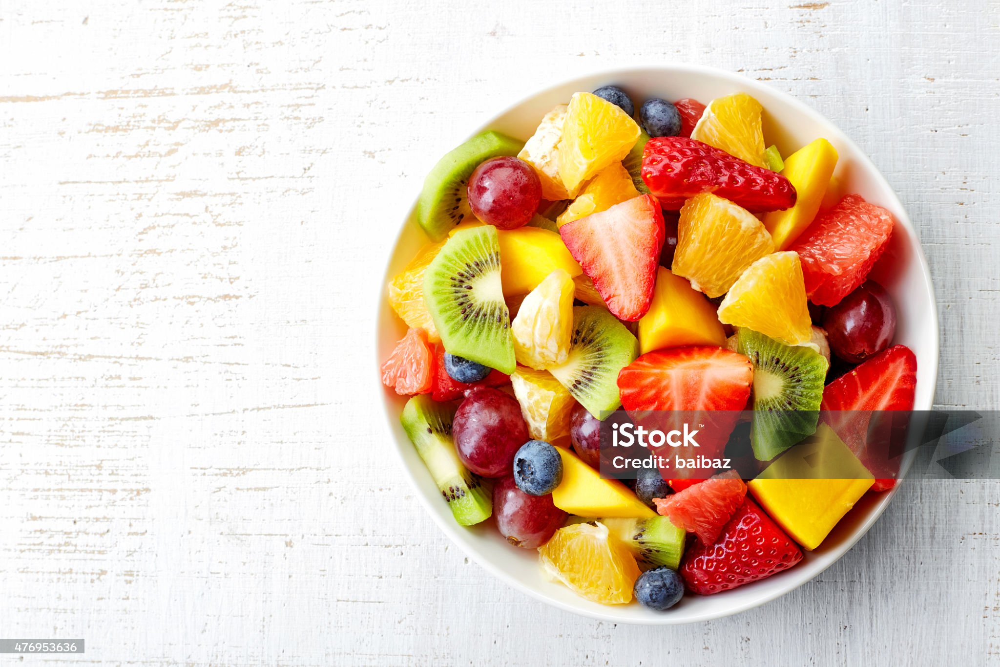 Bowl of healthy fresh fruit salad on wooden background. Top view.